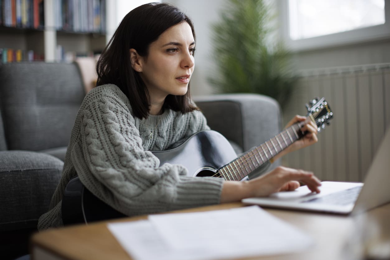 Young woman practicing guitar while attending an online music class